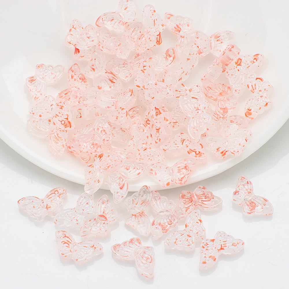 A pile of small, translucent pink glass butterfly beads for jewelry making.