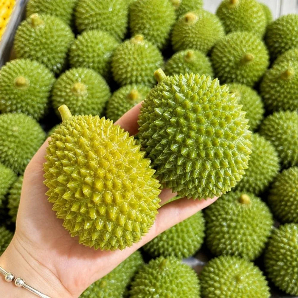 A hand holds a bright green crunchy durian squeeze toy with a textured surface against a background of similar green fruits.