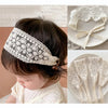 Close-up of a baby wearing a white floral lace headband and separate lace fabric accessories.