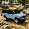 A light blue RC 4WD crawler truck is shown driving off-road over rocks and dirt.