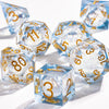 A collection of clear blue liquid core polyhedral dice with gold galaxy finish scattered on a white surface.