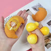 A hand holds an orange squishy hamburger stress ball and a yellow squishy ball against a light background.