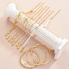 A collection of gold and pearl bracelets, including a sign bracelet and rings, displayed on a white column.