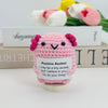 A pink crocheted pencil ornament with a face and ears, sitting on a wooden base.