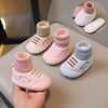 A hand holds a pair of pink and light blue knit bear booties for a baby's first steps, with additional pairs displayed nearby