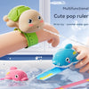 A cute, light brown turtle-shaped pop ruler water gun is being used to spray water onto a pink turtle in a glass of water.
