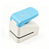 A light blue lever action embosser tool with a white base and a square embossing plate.