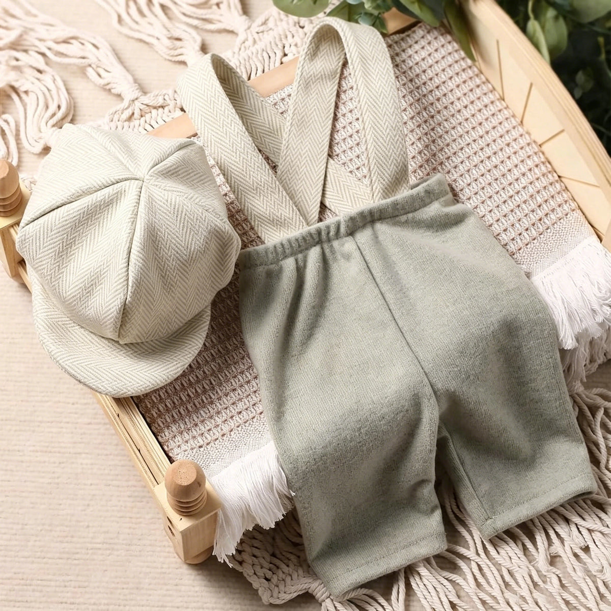 A set of a light green knit romper and matching newsboy cap laid on a beige woven background.