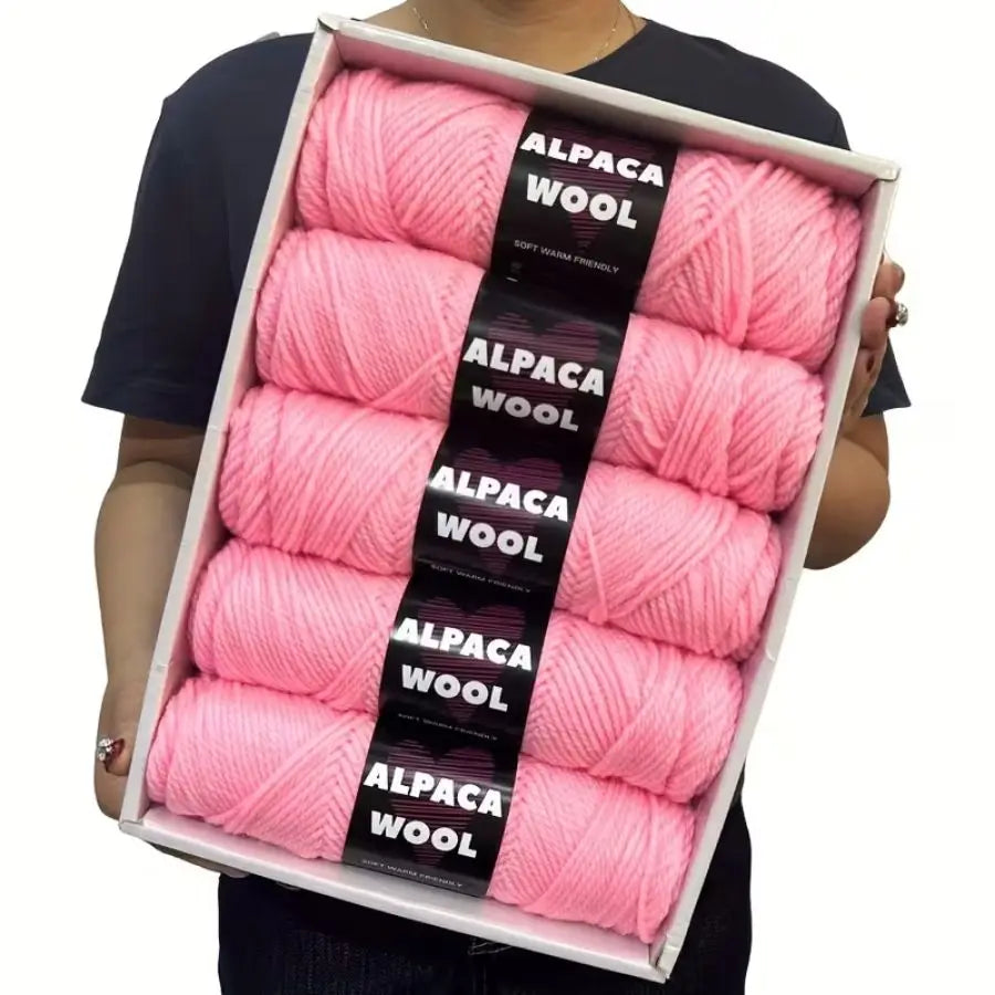 A box containing five skeins of pink alpaca wool yarn for knitting and crochet.