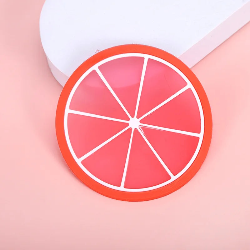 A round, sliced orange fruit pattern coaster with white lines rests on a pink surface next to a white box.