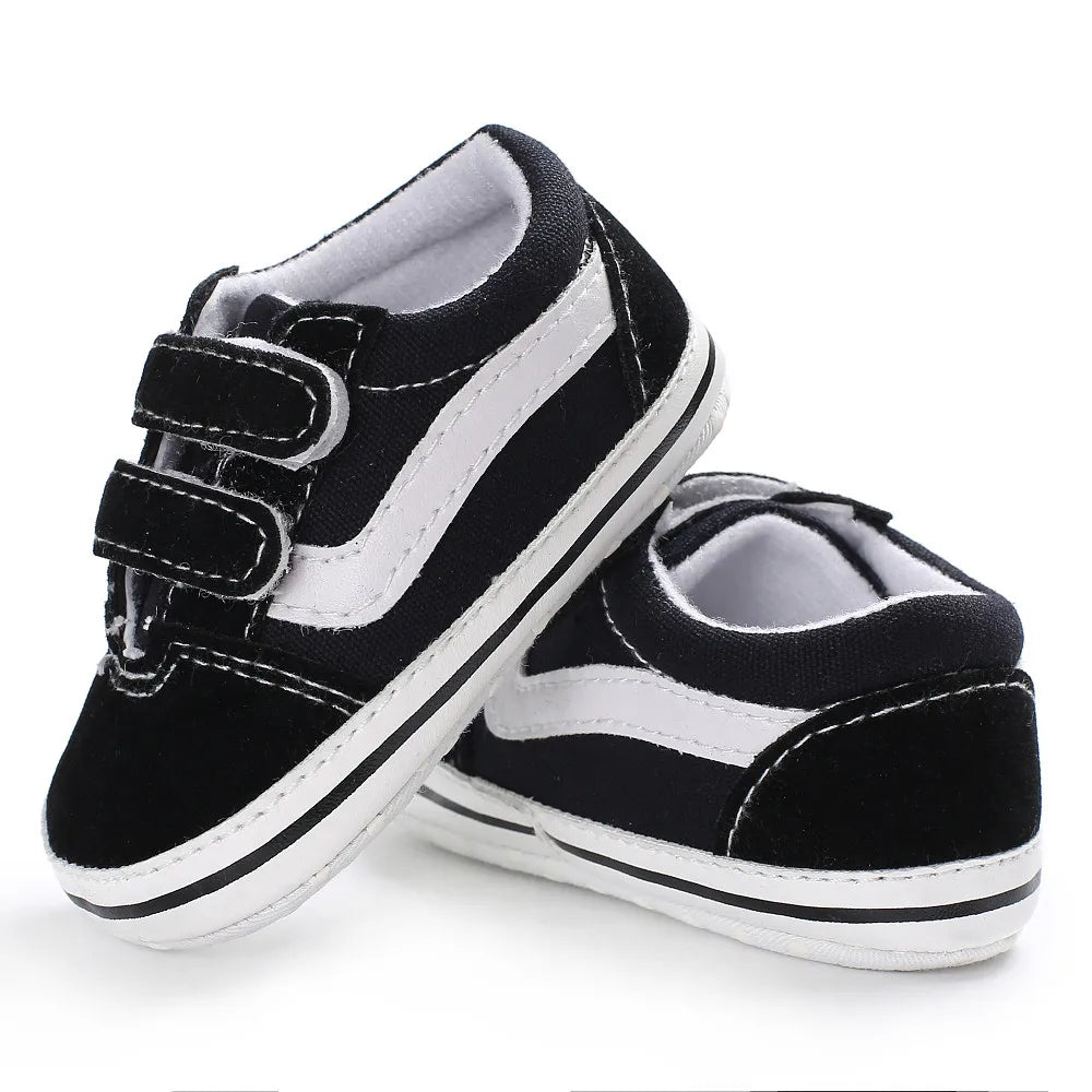 A pair of black and white striped canvas sneakers for babies shown from the side.