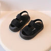 A pair of black toddler soft-soled sandals for boys and girls resting on a light beige surface.