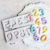 A silicone mold set featuring numbers 1 through 9 in pastel colors arranged on a white decorative plate.