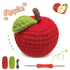 A red crocheted apple with a green leaf and a brown stem, next to yarn and a crochet needle.