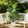 Artificial areca palm plant in a white decorative pot sitting on a wooden porch with white chairs.