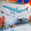 A blue geometric shark banner and hanging garland decorate a white wall for a birthday celebration.