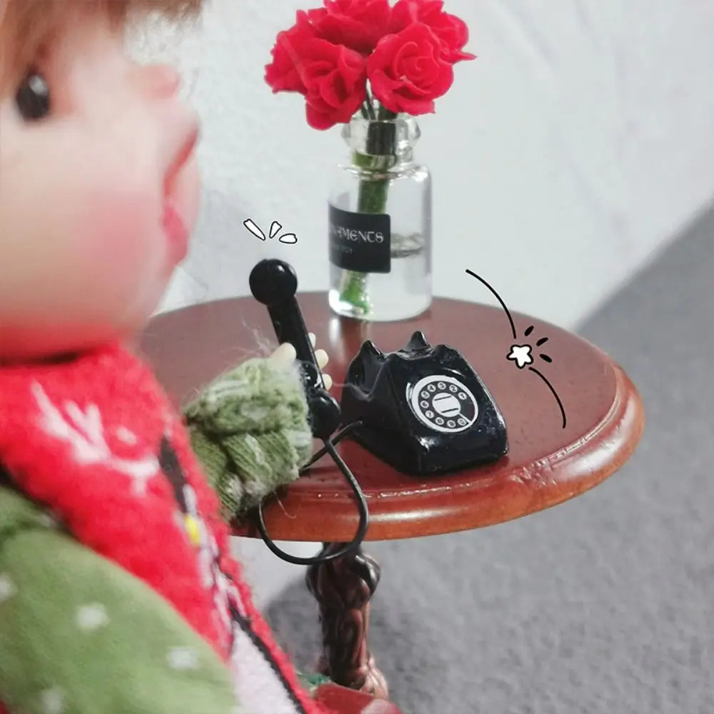 A vintage rotary telephone miniature is placed on a wooden table next to a vase of red roses.
