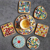 A collection of colorful mosaic glass tiles in various shapes and sizes arranged on a gray surface.