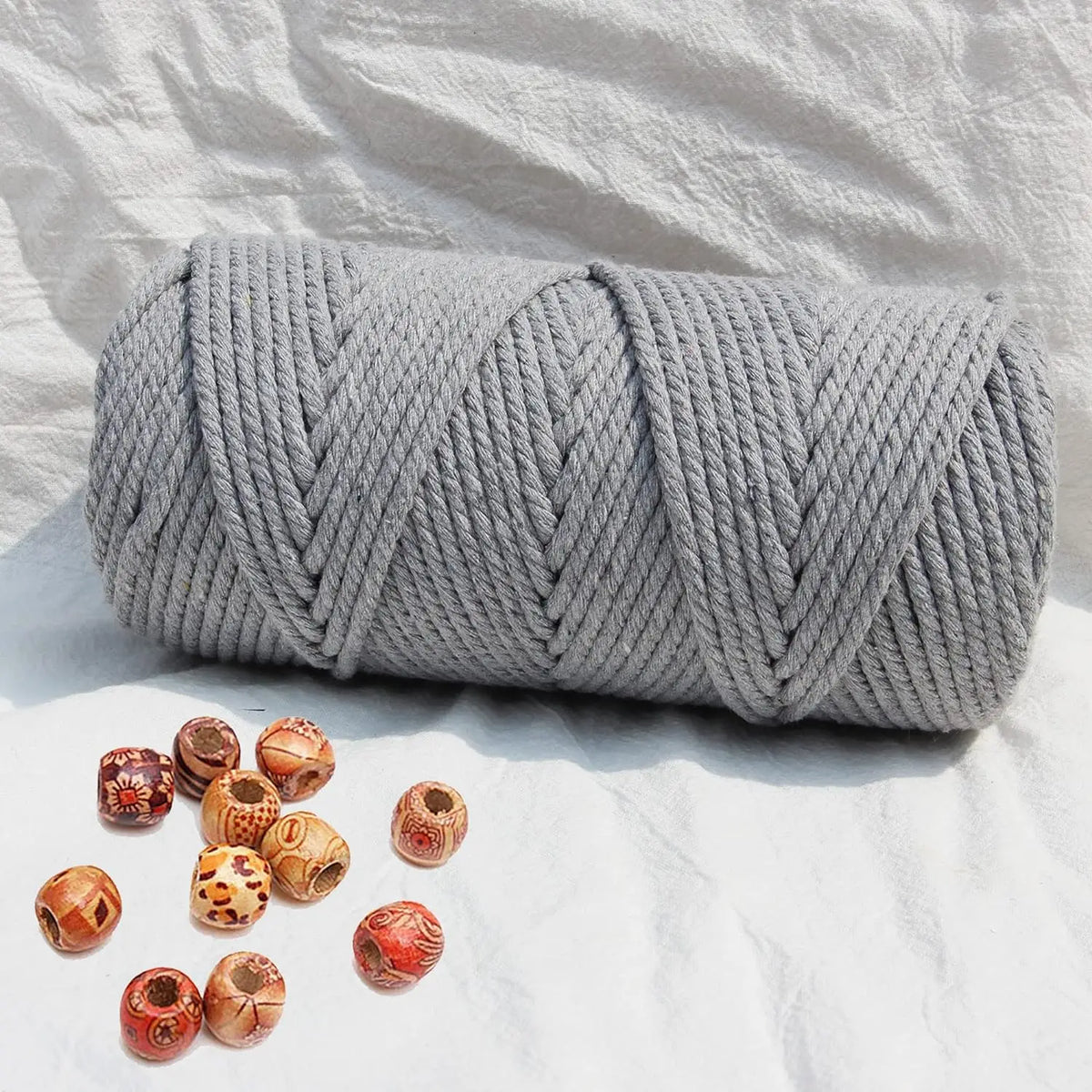 A tightly coiled gray natural cotton macrame rope for crafts and decor resting on a white fabric background.