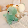 A soft green dinosaur plush toy and a cream-colored dinosaur plush toy are displayed on a white surface.