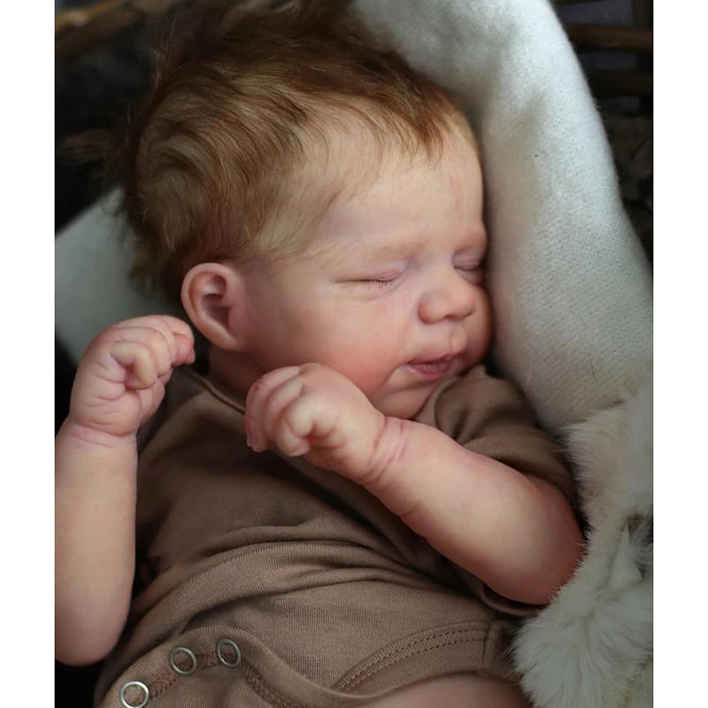 A close-up photo of a newborn reborn baby doll with rooted hair sleeping, wrapped in a soft fabric.