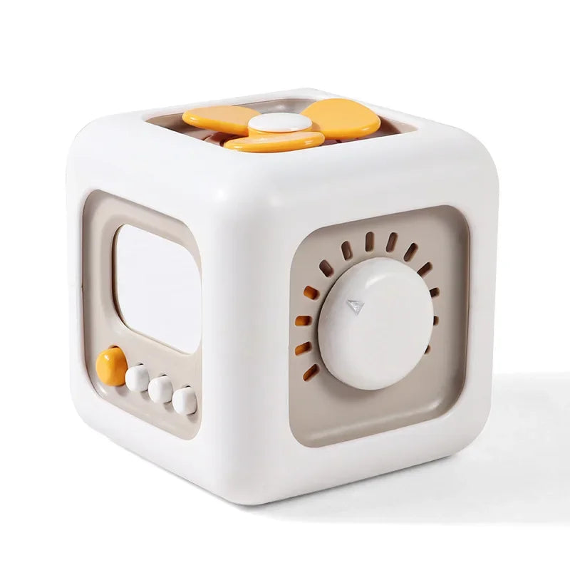 A white cube sensory toy with a translucent lid containing six yellow and white discs for toddlers.