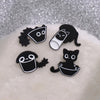 A set of four black cat enamel pins displayed on a white, fluffy surface.