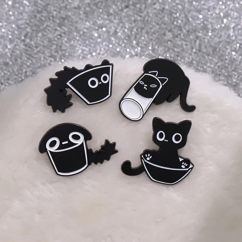 A set of four black cat enamel pins displayed on a white, fluffy surface.