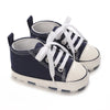 A pair of navy blue and off-white canvas baby shoes with white laces shown from the side.