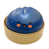 A blue, round squishy toy shaped like a dumpling is resting in a light beige dish.