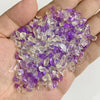 A handful of tumbled amethyst and quartz stone chips in various shades of purple and clear white.