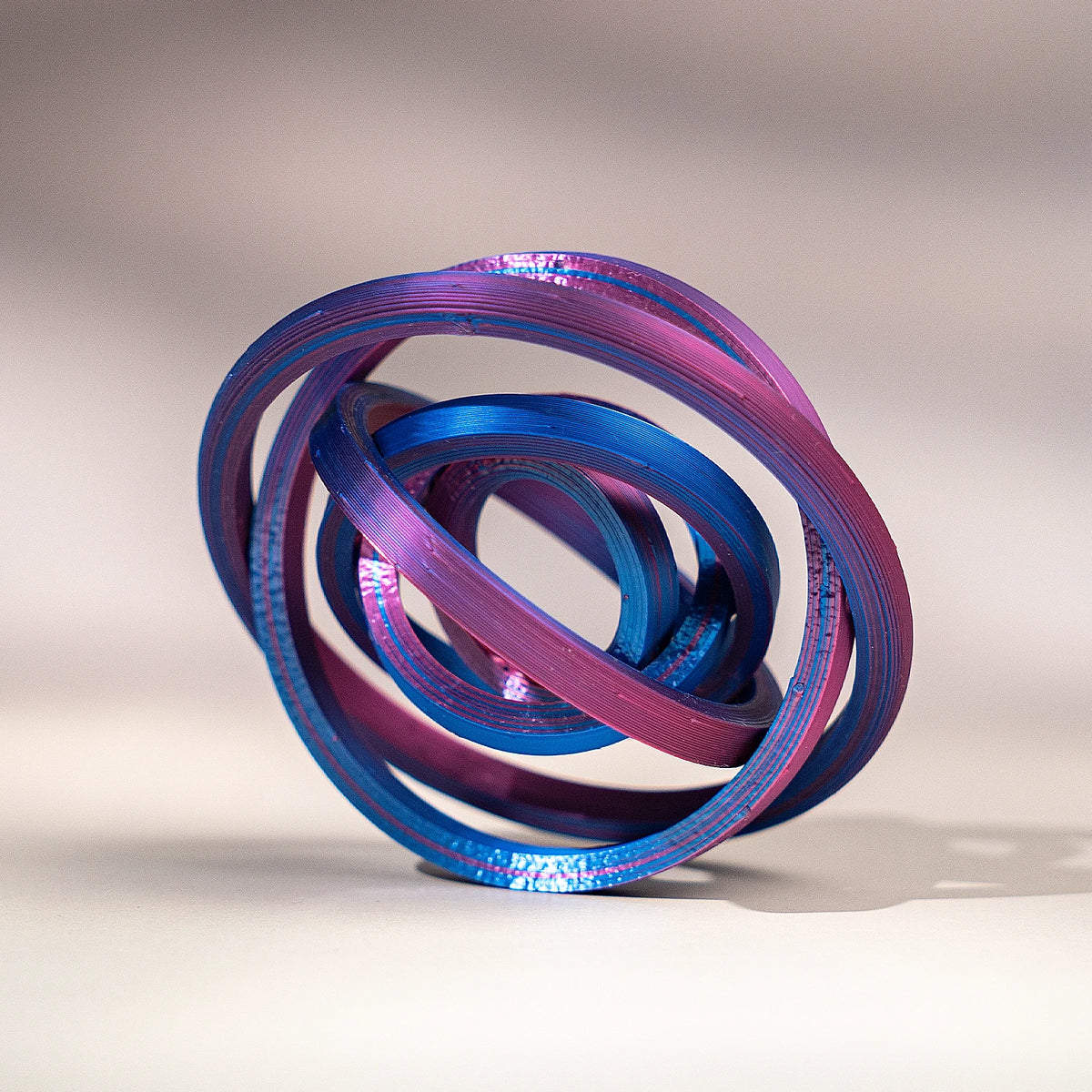 A close-up of a 3D printed rainbow spinner ring with iridescent purple and blue bands, shown in a circular motion.