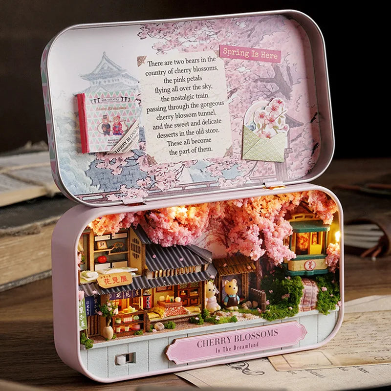 A pink wooden miniature dollhouse theater kit featuring a detailed cherry blossoms scene with a shop and figures.