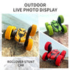 Outdoor live photo display of a yellow and black rollover stunt car with orange wheels on a rock.
