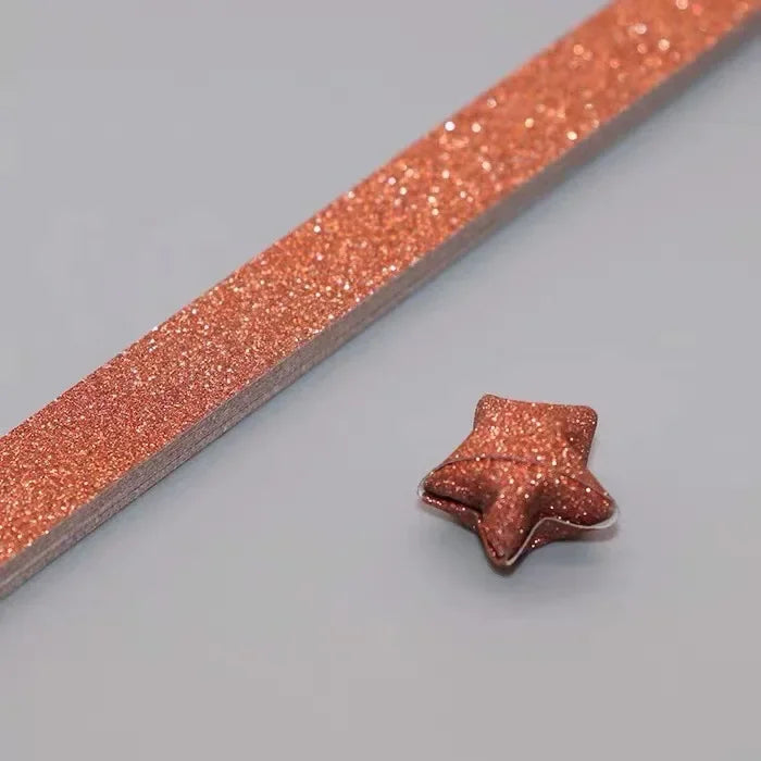 A close-up of a narrow strip of rose gold glitter paper with a star shape cut out on one end.