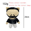 A plush doll resembling a bear with a black face and mustache, wearing a black shirt and light pants.