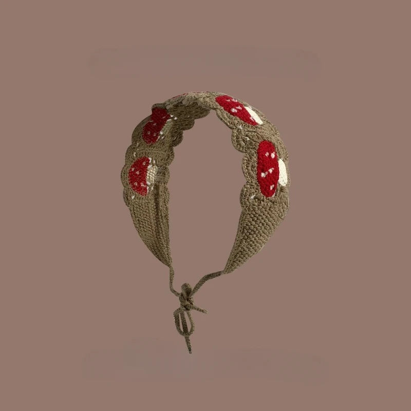 A handmade strawberry crochet headband with a wide elastic band against a solid brown background.