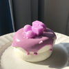 A pink and purple glazed cream puff with small pastel cubes on a white plate.