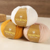 Three balls of Merino wool yarn in white, yellow, and pink colors with branded labels
