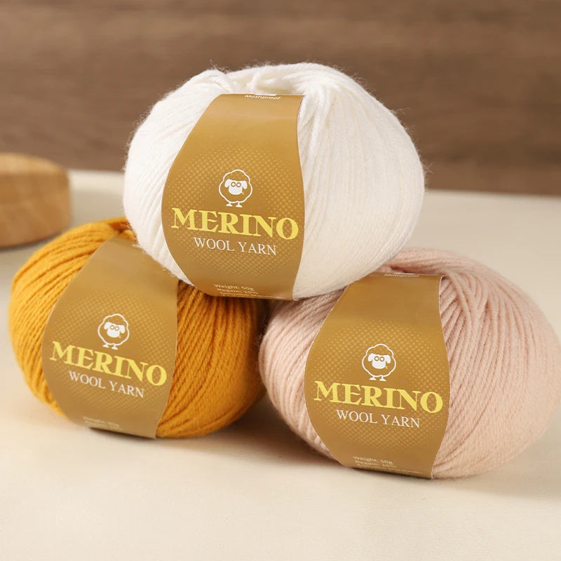 Three balls of Merino wool yarn in white, yellow, and pink colors with branded labels