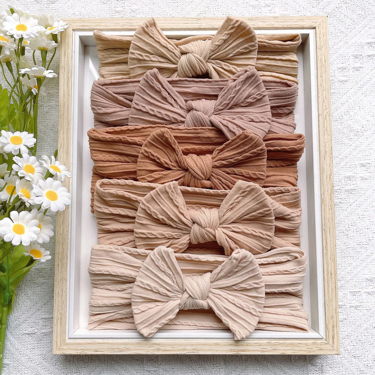 A display of five beige knitted bow baby headbands arranged in a wooden frame.