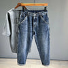 A pair of vintage loose fit denim harem jeans folded and displayed on a hanger against a gray wall.