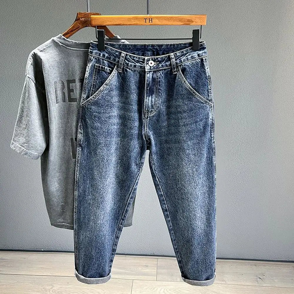 A pair of vintage loose fit denim harem jeans folded and displayed on a hanger against a gray wall.