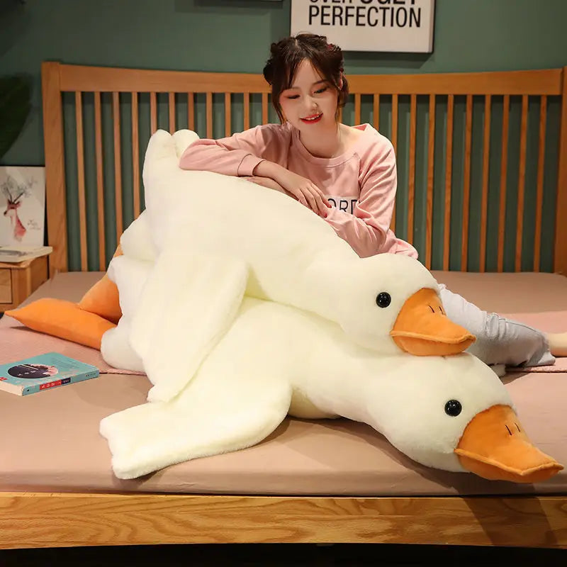 A woman is sitting on a bed with an extra-large white plush goose pillow.