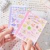 A hand holds a pink and purple die-cut sticker book featuring stars, a duck, and other cute cartoon designs.