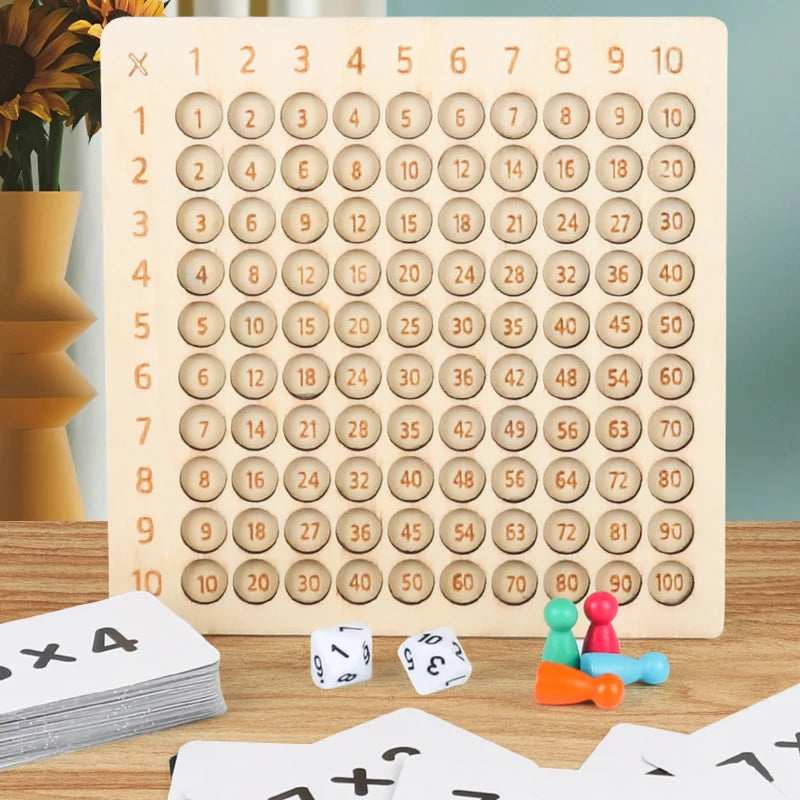 A wooden multiplication board game with numbered tiles laid out on a light wood surface next to playing cards.