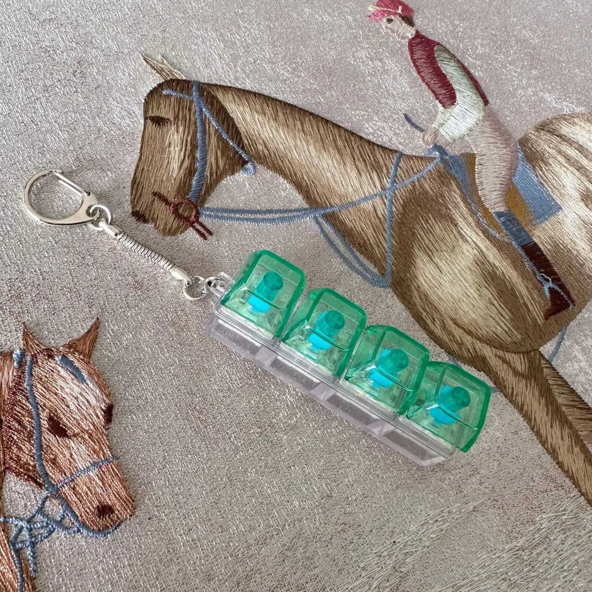 A horse figurine is shown next to a clear acrylic keycap fidget keychain with four green buttons.
