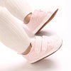 Pink soft-sole baby first walkers worn on a person's foot.