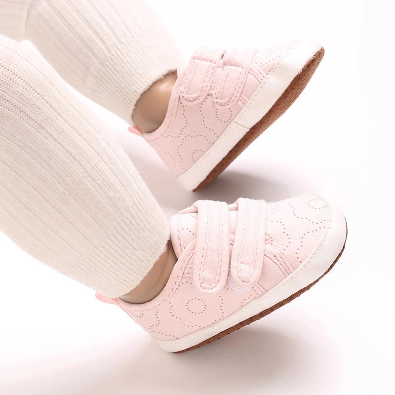 Pink soft-sole baby first walkers worn on a person's foot.