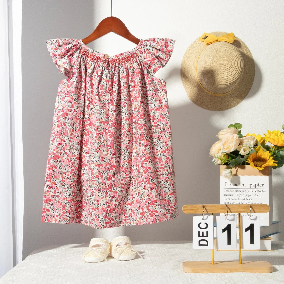 A pink floral smocked summer dress for girls with flying sleeves displayed on a hanger.